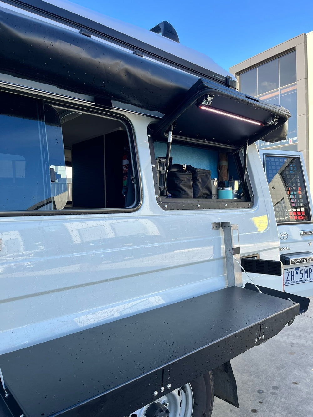 White Troopy with the side hatch lifted on lit storage and a fold-down table below