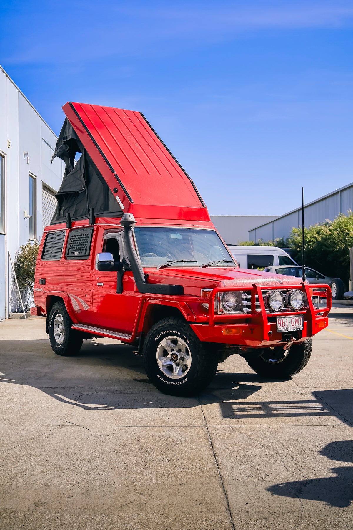 Red Troop Carrier with its red pop-top roof raised, parked on a concrete yard