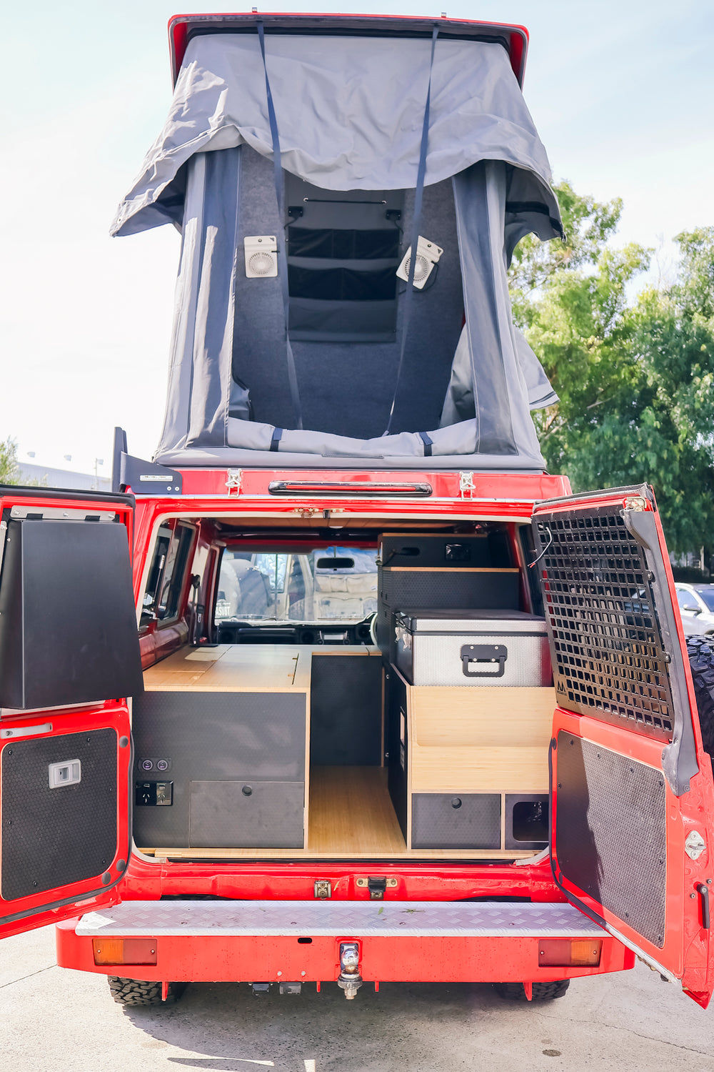 Red Troopy from the rear with the pop-top raised and barn doors open, showing the fitted cabinetry